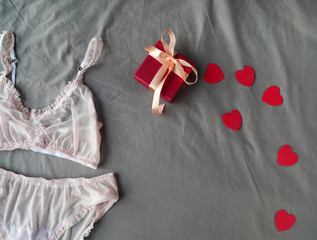 Top view of red gift box, hearts and women's pink underwear at grey bed