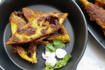Marinated Pomfret fried fish or Indian Spicy fish fry garnished with onion and coriander on iron skillet griddle, selective focus with copy space.