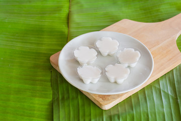 Colorful of Thai coconut jelly in small plastic cup on wooden plate with green banana leave background. Thai dessert.