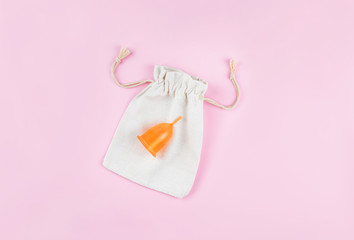 Orange menstrual cup on white cotton bag on pink background. Woman's health and environmentally friendly feminine hygiene product concept.