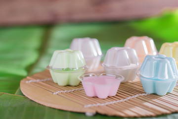 Colorful of Thai coconut jelly in small plastic cup on wooden plate with green banana leave background. Thai dessert.
