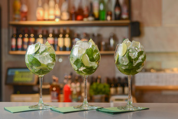 Fresh drinks Mojito with lime and ice in three clear glasses on a table in bar. Copy space.