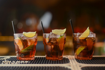 Fresh drinks with lemon and ice in three clear glasses on a table in bar.