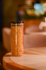 Macaroni in glass jar on a light wooden table with blurry background.