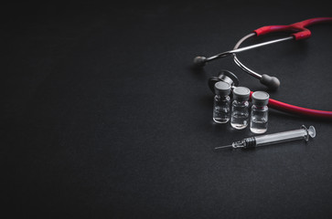 Stethoscope, vials and syringe on black background. Selective focus and copy space