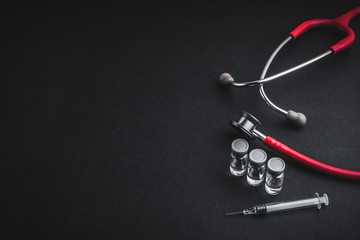 Stethoscope, vials and syringe on black background. Selective focus and copy space