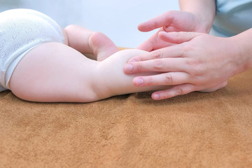 Professional doctor masseur making massage to baby on leg in clinic, legs closeup view. Therapist's hands gently massaging baby's leg. Medicine, cure, babycare concept. Hypertonicity problem.