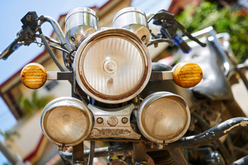 A close-up low angle view of the front head lights of an old, dirty and rusty motorcycle parked in a small town in the Philippines