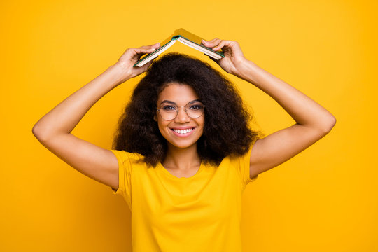 Close-up portrait of her she nice attractive lovely funky comic cheerful cheery wavy-haired girl fooling holding book over head isolated on bright vivid shine vibrant yellow color background