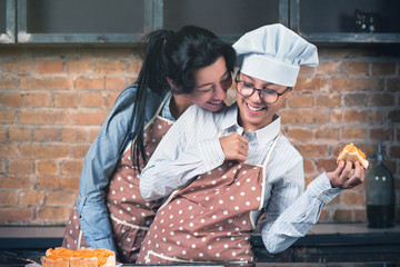 Cheerful and laughing mom and daughter baked a cake in the kitchen. A woman is standing at the...