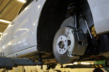 A modern luxury car at a service station is lifted on a lift for repair.  Front brake disc,...