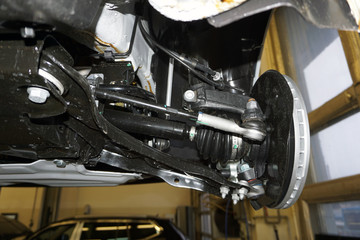 Elements and design of the front suspension of a modern car. Drive shaft with protective cover, suspension arm, steering rod and steering tip, wheel bearing housing, brake tubes and hoses.