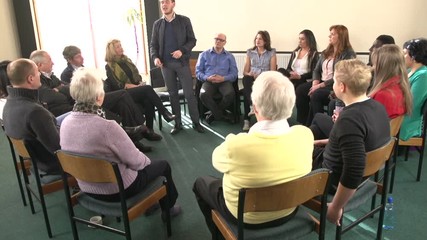 Group of people sat in Circle introducing themselves to each other. One young man talks while others listen. Crane Shot