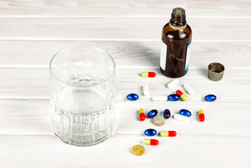 Close-up of bright colored medical tablets, a bottle of medicine and capsules with medicines and a glass of water. Scattered on the table Pills from the first-aid kit box. Toned. Copy space