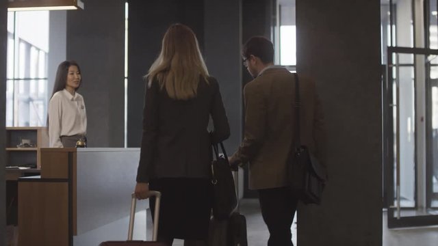 Tracking shot of man and woman with suitcases walking up to reception desk and checking out of hotel