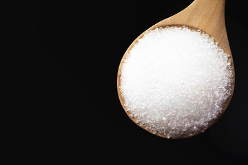 Closeup sugar with a wooden spoon on black background from top view.