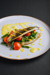 Dorado fillet with green beans, cherry tomato and curry sauce on a black background