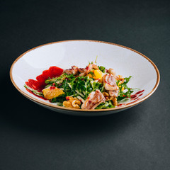 Warm salad with duck breast, orange pulp, arugula, walnuts and cranberry sauce on a black background