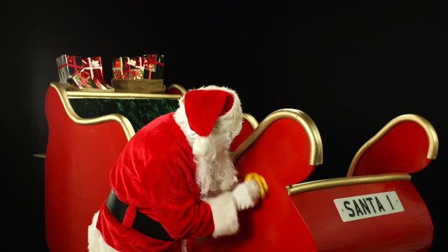 Santa Claus polishing his sleigh with a cloth. Father Christmas preparing for the big day on a black background. Stock Video Clip Footage