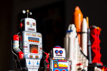 Vintage tin toy robot looking into the future of space exploration with rocket in background,...