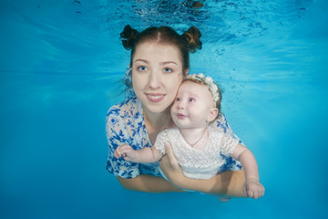 Mom with a small daughter swim underwater in a swimming pool