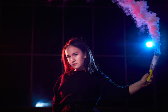 Teenage chubby girl with colored smoke torch in hand during photoshoot with colored smoke at night and black background