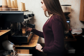 Professional espresso coffee machine in a cafe. Barista pours coffee into a paper cup. Hands of a girl in the process of making coffee.