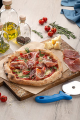 Delicious fresh pizza on table.  Pizza with prosciutto (parma ham), arugula (salad rocket) and parmesan, served on a wooden table for dinner, close up. Italian cuisine.
