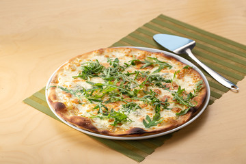 Delicious fresh pizza on table. Pizza with prosciutto (parma ham), arugula (salad rocket) and parmesan, served on a wooden table for dinner, close up. Italian cuisine.