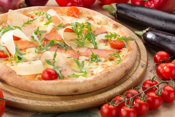 Delicious fresh pizza on table. Pizza with prosciutto (parma ham), arugula (salad rocket) and parmesan, served on a wooden table for dinner, close up. Italian cuisine.