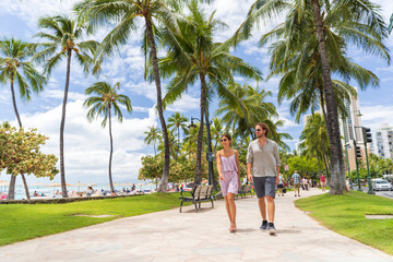 Fototapeta na wymiar Honolulu city travel tourists couple walking on Waikiki beach boardwalk visiting Oahu island, USA summer travel holidays. Happy man and woman lifestyle.