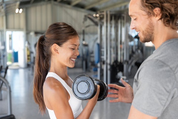 Fototapeta premium Gym workout personal trainer man helping woman having the right body posture to lift dumbbell weights. Exercise fit lifestyle.