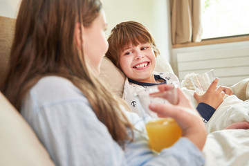 Obraz na płótnie Canvas Kinder trinken zusammen Orangensaft im Bett