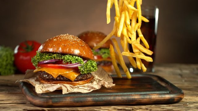 Super Slow Motion Shot of Fast Food Concept. Falling French Fries on Wooder Cutting Board next to the Fresh Hamburger at 1000fps.