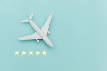 Simply flat lay design miniature toy model plane and 5 stars rating on blue pastel colorful trendy background. Travel by plane vacation summer weekend sea adventure trip journey ticket tour concept.