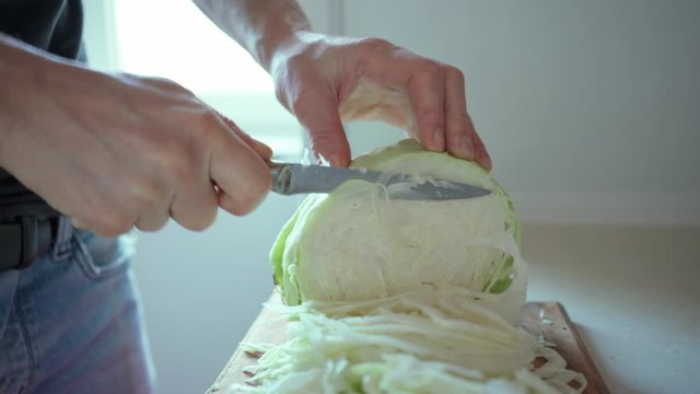 man Cutting Cabbage With A Cleaver Knife for a vegetarian salad. Closeup of male hands slicing a piece of cabbage on a wooden board