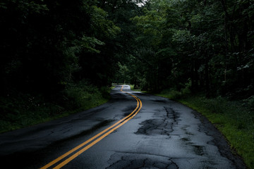 Winding road on a rainy day guiding through the Green Mountains of Vermont. Curves and damaged pavement can be quite challenging on a rainy day.