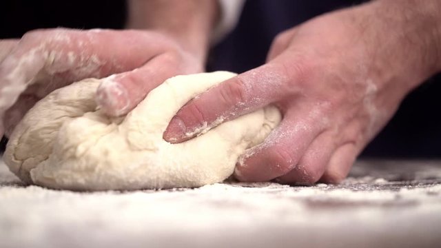 Baker kneading dough in flour on table