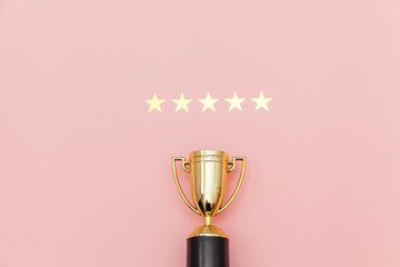Fototapeta Simply flat lay design winner or champion gold trophy cup and 5 stars rating isolated on pink pastel background. Victory first place of competition. Winning or success concept. Top view copy space. obraz