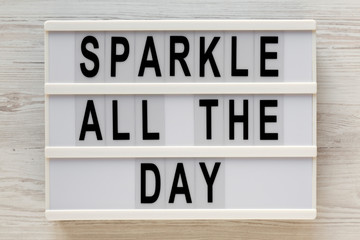 'Sparkle all the day' words on a lightbox on a white wooden surface, top view. Overhead, from above, flat lay. Close-up.