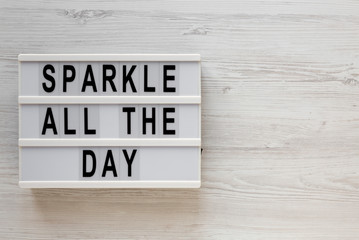 'Sparkle all the day' words on a lightbox on a white wooden surface, top view. Overhead, from above, flat lay. Copy space.