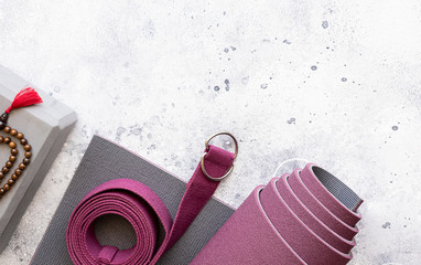 Yoga accessories. Rolled exercises  mat, wooden mala beads, yoga  blocks and belt on grey concrete...