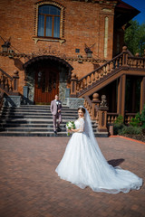 The bride in a white wedding dress and groom in a suit on the background of a brick building with large steps