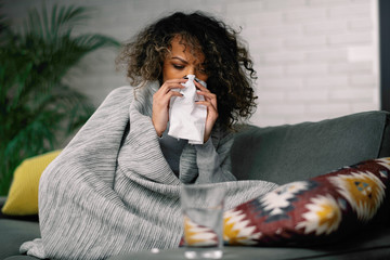 Sick woman at home. Young african woman laying on sofa she is sick having fever. 