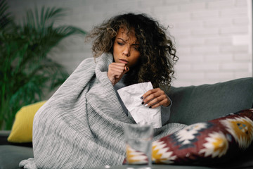 Sick woman at home. Young african woman laying on sofa she is sick having fever. 