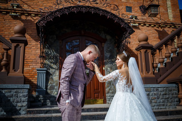The bride in a white wedding dress and groom in a suit on the background of a brick building with large steps