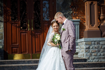 Fototapeta premium The bride in a white wedding dress and groom in a suit on the background of a brick building with large steps