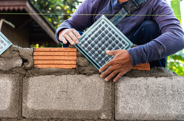 Hands of construction worker installing glass block between bricks on construction site
