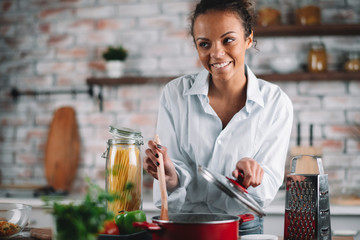 Young woman in kitchen. Beautiful mixed race woman cooking pasta. 