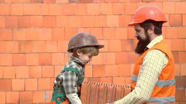 Little son bricklayer building a wall from bricks or stone blocks. Son helper. Child with her parent in Hard Hat Playing Building Blocks. Little son helping his father with building work.